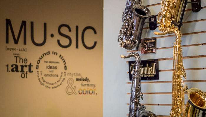 Four saxophones with a music quote on the wall behind them.
