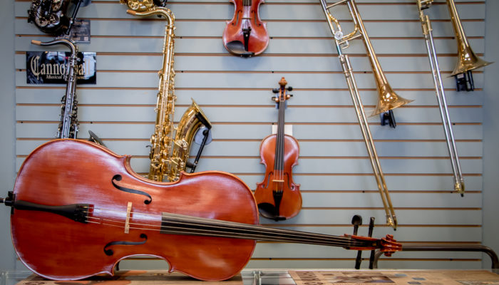 Cello on a cabinet on its side with other band and orchestra instruments hung behind it.