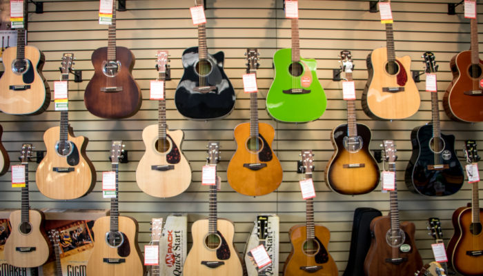 Acoustic guitars in different colors displayed on wall.