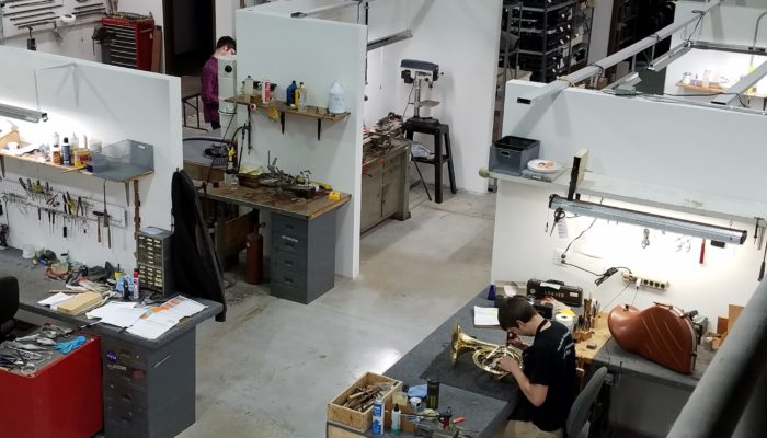 Overhead view of repair shop with technician working on a French horn.