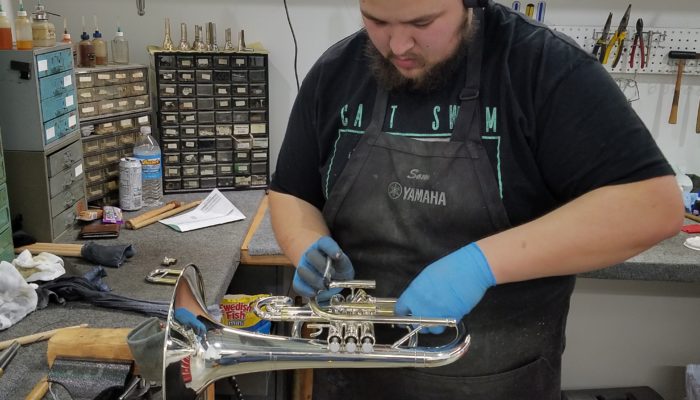 Repair tech repairing a silver trumpet