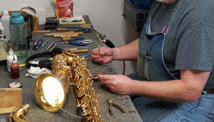 Repair technician using a light tester to check pads on a saxophone.