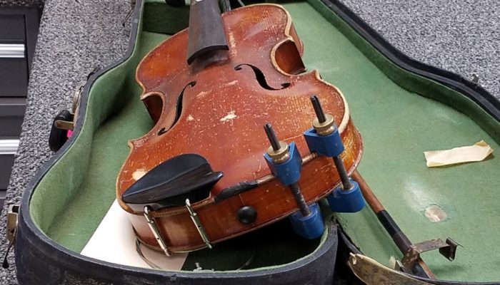 Violin without bridge or strings sitting on a green case.