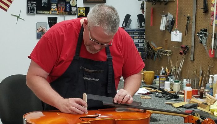 Repair technician replacing the bridge on a cello.