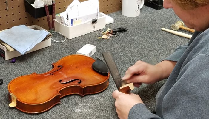 Repair technician working to repair the neck of a violin which has come apart.