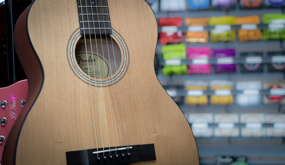 Fender acoustic guitar and music products blurred in background.