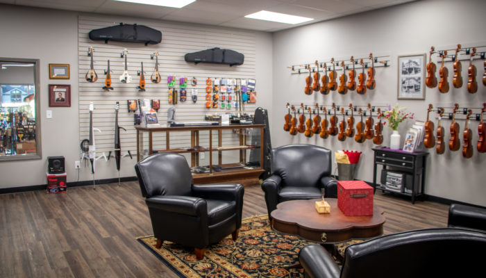 Room with seating area and violins and string accessories  displayed on wall.