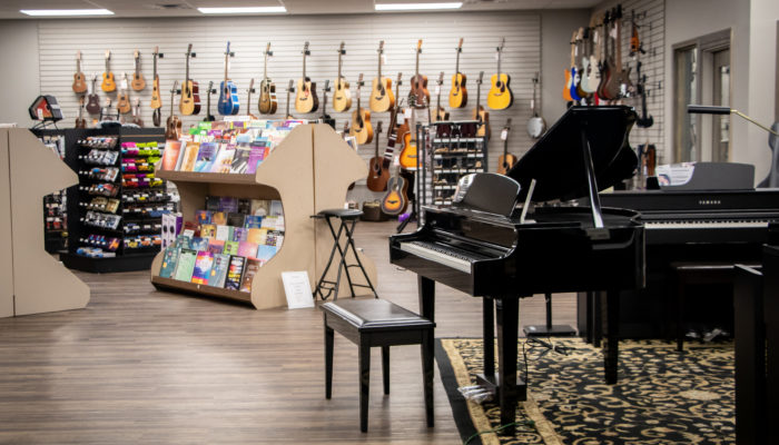 Yamaha digital piano with bench and selection of guitars behind it.