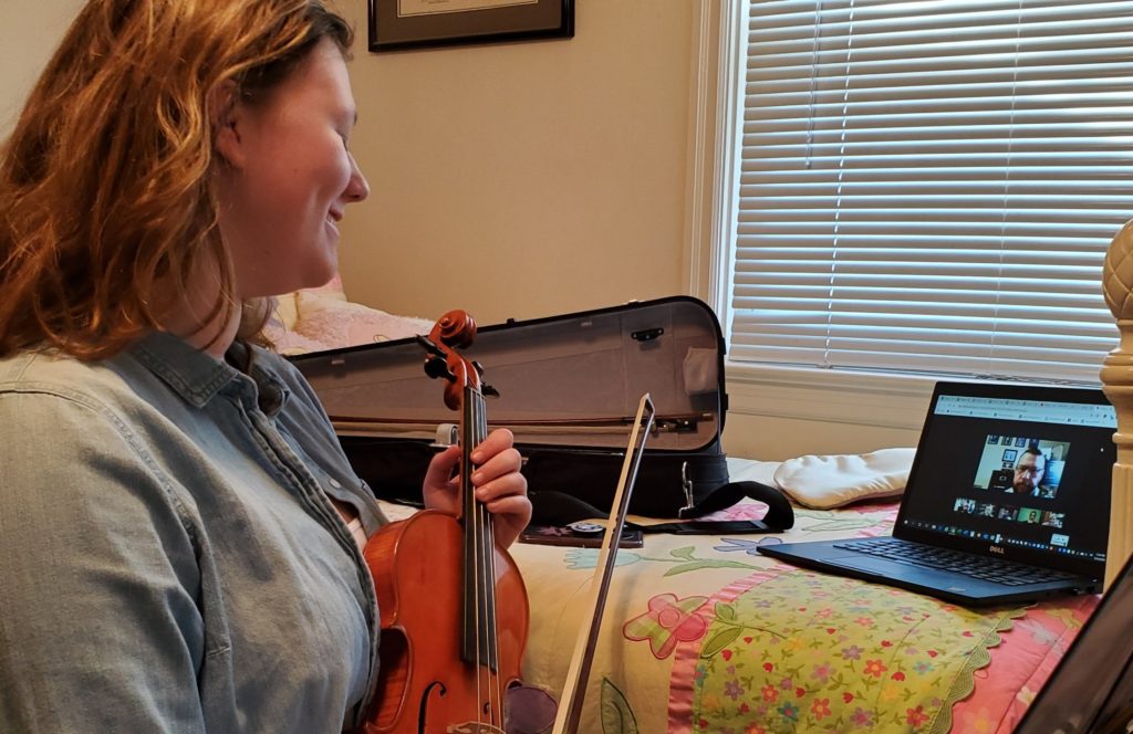 girl holding violin while listening to teacher during an online lesson