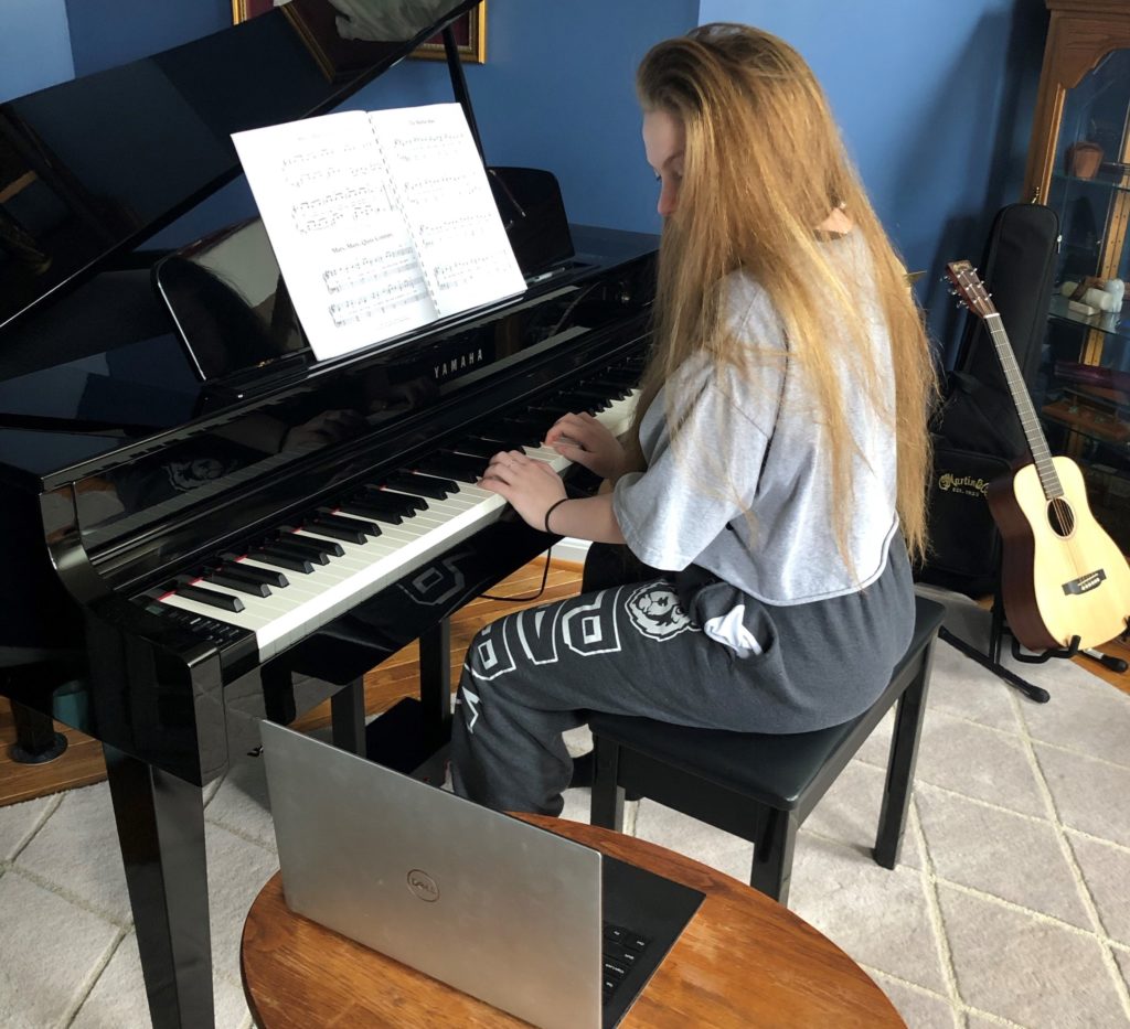 Girl sitting at piano taking online music lesson