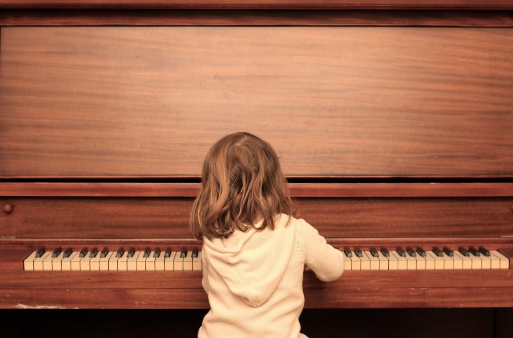 Young girl sitting in front of a brown upright piano