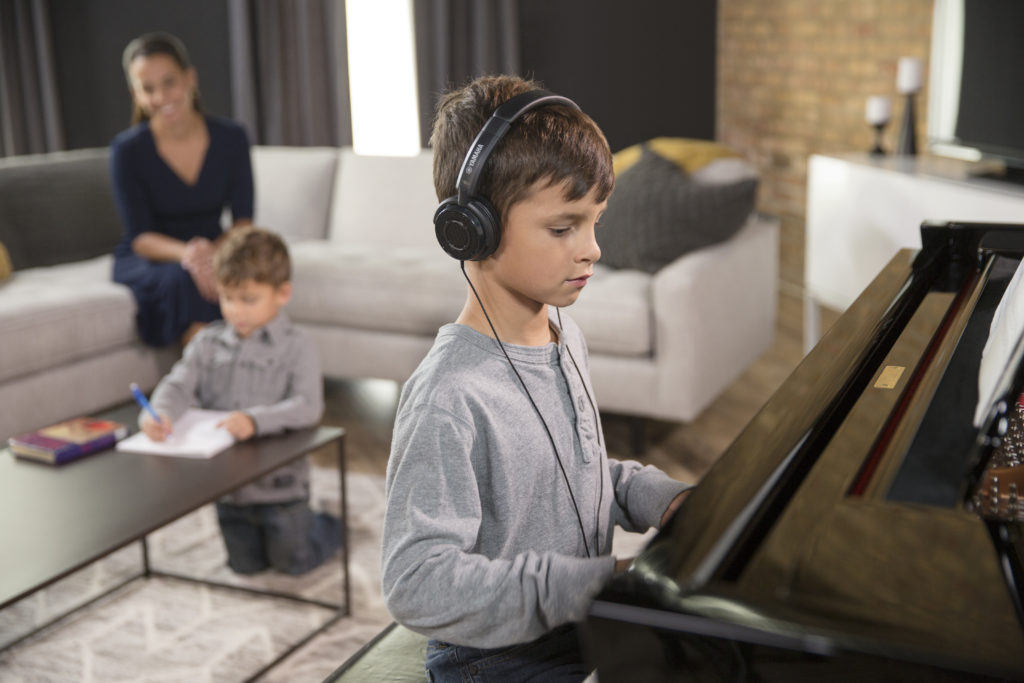 child with headphones playing piano with family in the background