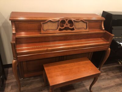 Closed view of a Yamaha M405 cherry upright piano, with the fallboard closed.