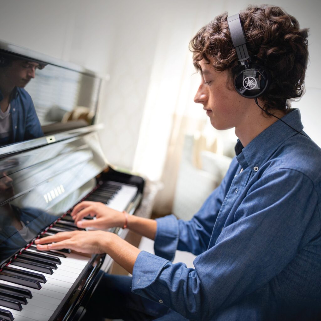 Image of teenage boy playing a Yamaha piano with headphones