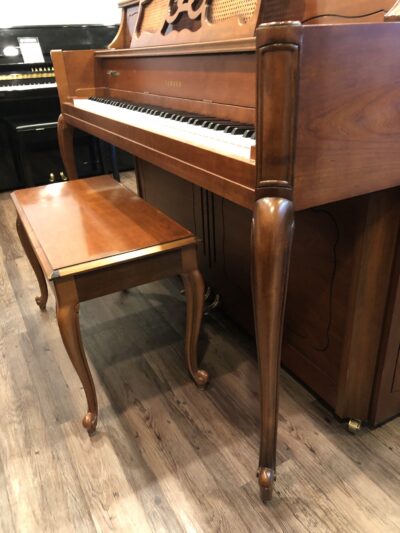 The Queen Anne style legs of a Yamaha M405 cherry console piano(#108632).
